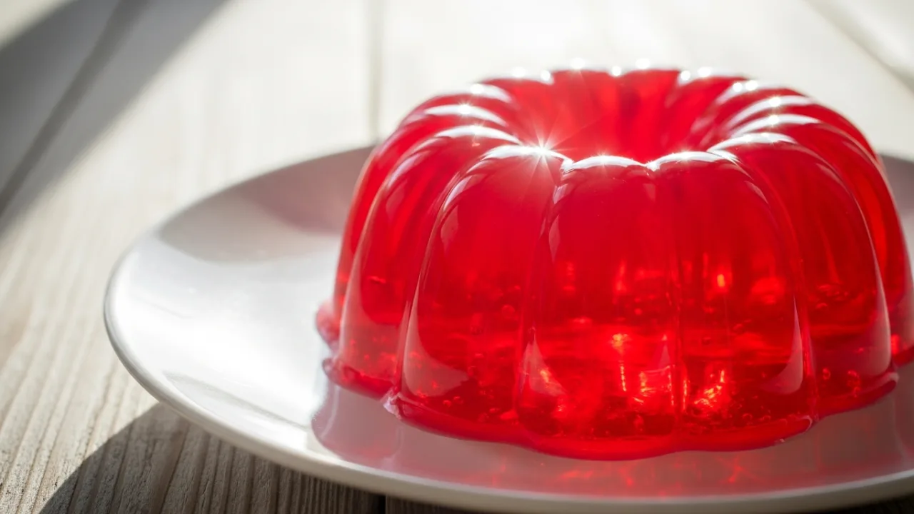 Gelatina vermelha brilhante e perfeitamente desenformada em um prato branco, mostrando sua textura lisa e firme.