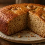 Banana cake fofinho e úmido com crosta dourada e fatia revelando miolo macio sobre mesa rústica