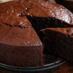 Bolo de chocolate amanteigado úmido e macio, com superfície rica em chocolate sobre mesa rústica