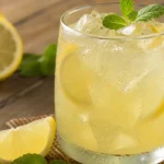 Suco de limão gelado em copo de vidro com limões cortados e gelo sobre mesa rústica