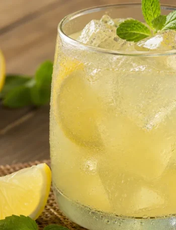 Suco de limão gelado em copo de vidro com limões cortados e gelo sobre mesa rústica