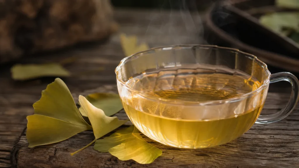 Chá de ginkgo biloba em xícara clara sobre mesa rústica, com folhas secas ao lado