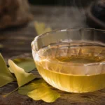 Chá de ginkgo biloba em xícara clara sobre mesa rústica, com folhas secas ao lado
