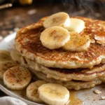 Panqueca de aveia com banana dourada, com rodelas de banana e canela sobre mesa rústica