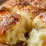 Pão doce fofinho com leite condensado, dourado e coberto com coco ralado sobre mesa de madeira