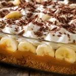 Torta banoffee na travessa com doce de leite, bananas, chantilly e chocolate sobre mesa de madeira